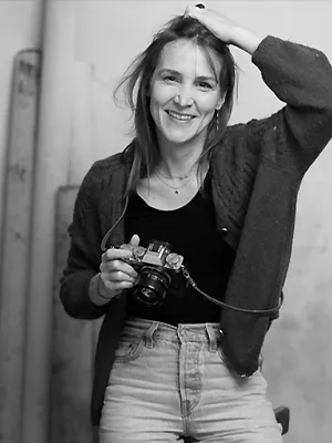 Portrait en noir et blanc de Candice Henin, photographe portrait à Paris, souriante avec son appareil photo.
