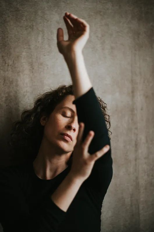 Portrait artistique d’une femme aux yeux clos, un bras levé et l’autre main posée délicatement sur son bras, dans une posture douce et poétique.