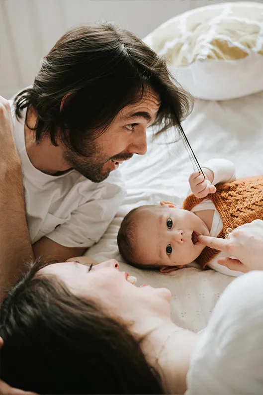 Photo de famille à domicile : moment de complicité dans le lit avec bébé.