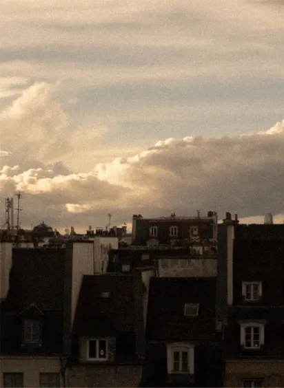 Vue photographique des toits de Paris en fin de journée, entre cheminées et toitures en zinc, dans une atmosphère poétique.